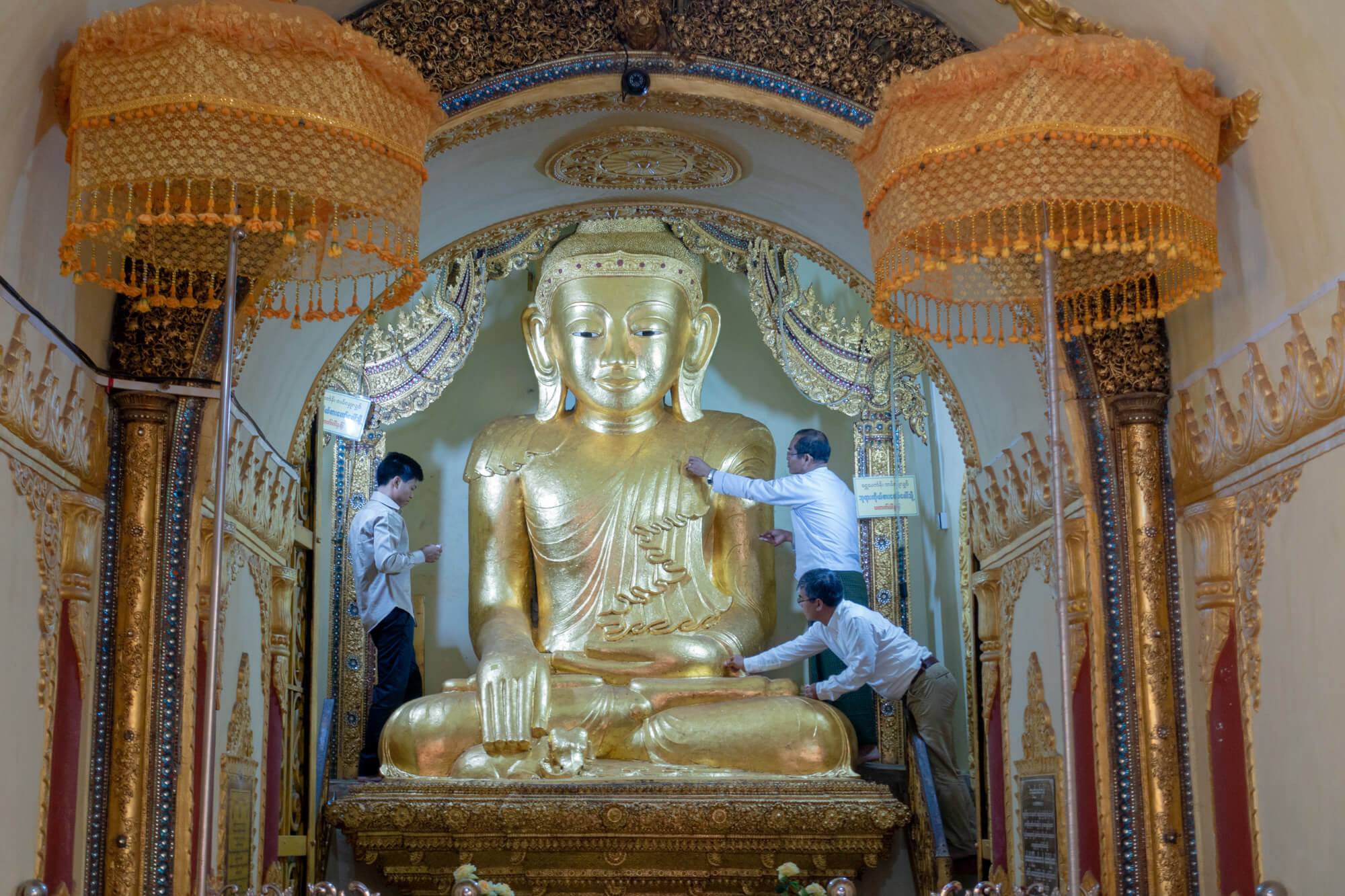 des Birmans posant des feuilles d'or sur le bouddha du monastère In Dein